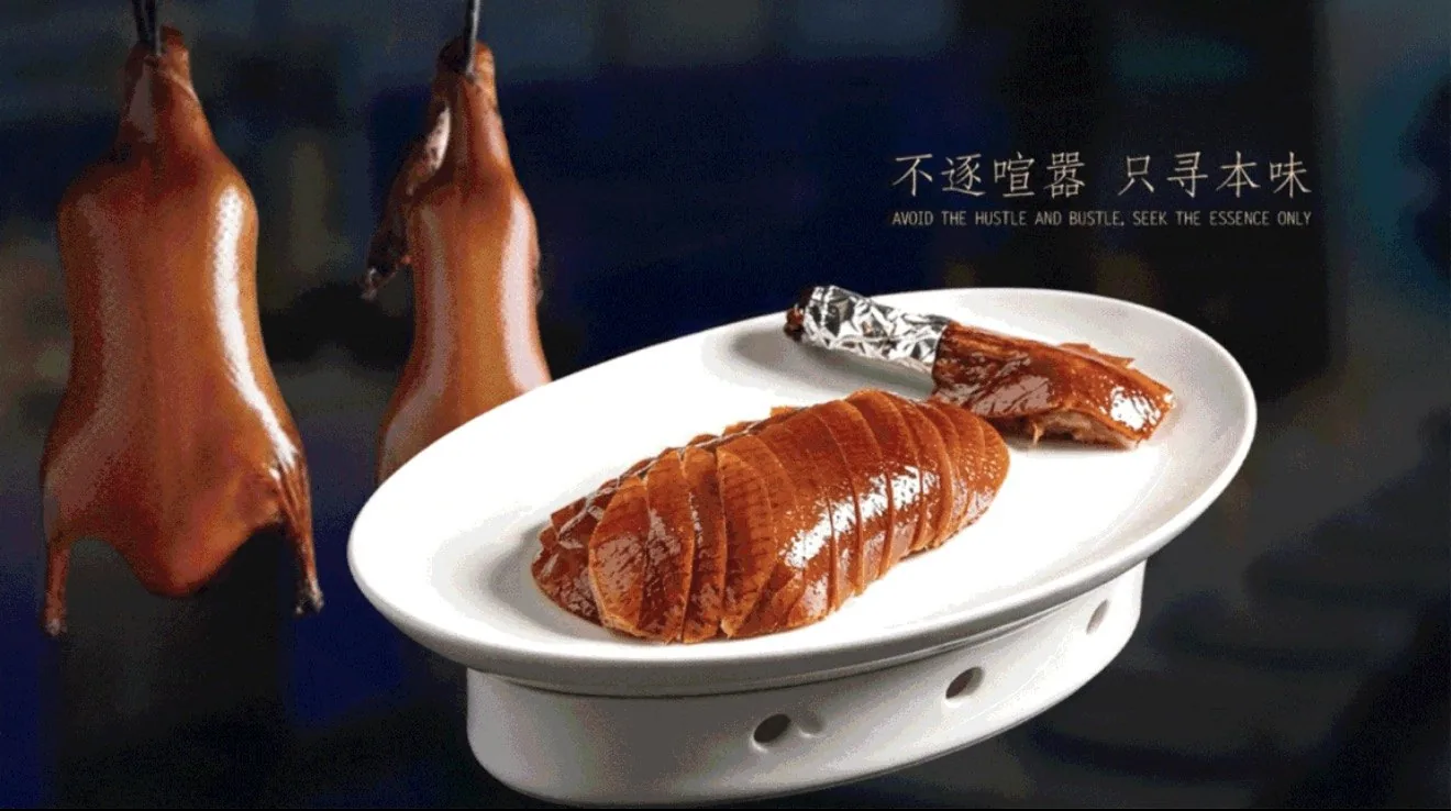 Sliced Peking duck plated in white porcelain, with two lacquered ducks hanging behind